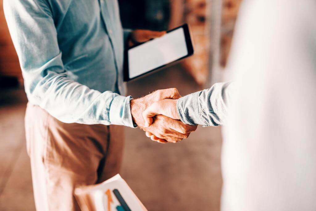 A 3PL partner and business owner shake hands in the warehouse.